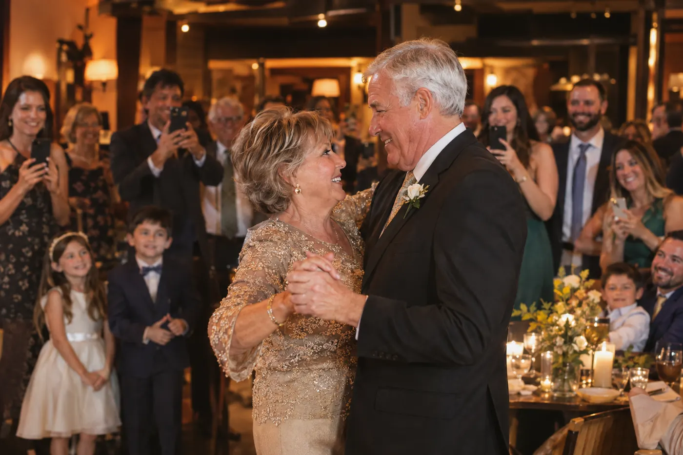 An older couple dancing at their anniversary dinner while family members film and photograph them with phones